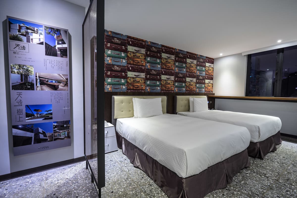 A hotel room with two beds, a wall decorated with suitcases, and a poster on the wall.