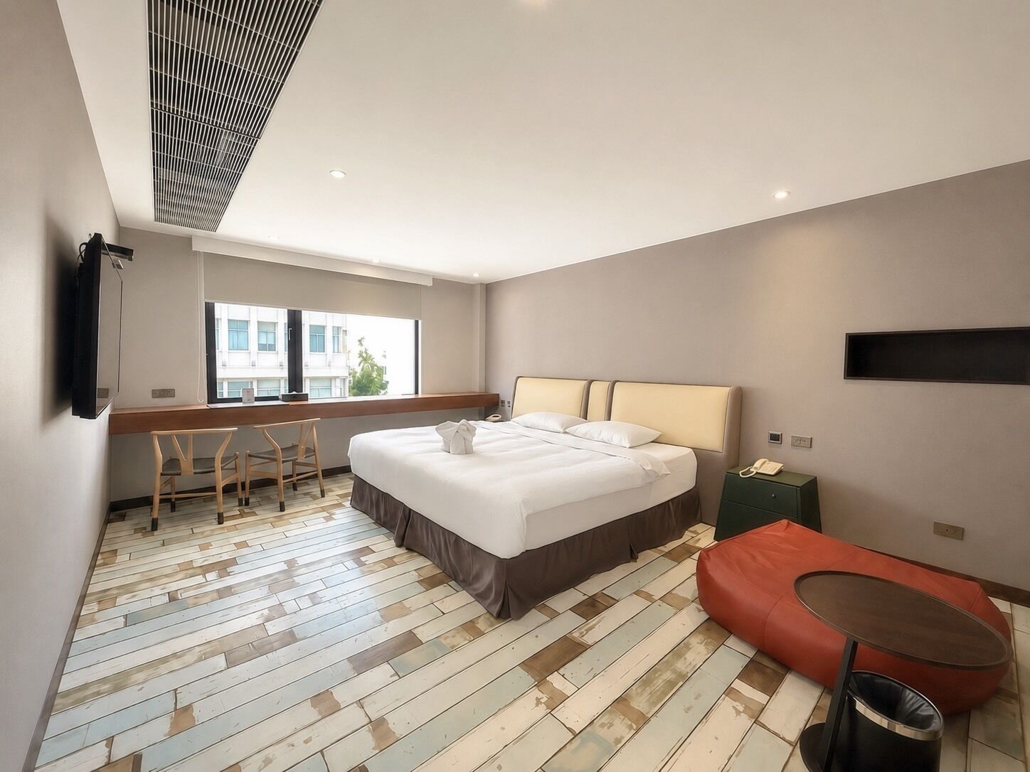 A modern hotel room with a large bed, a desk, a chair, a small table, and a sofa.