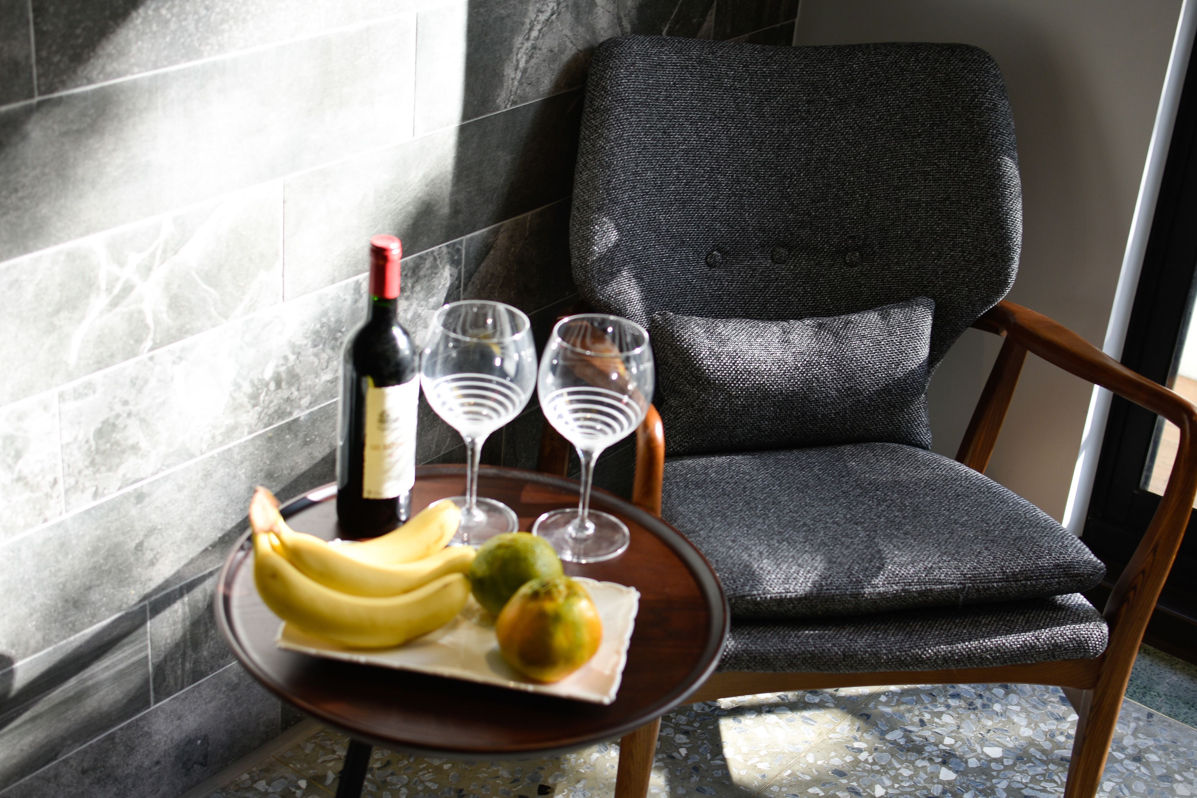 Uma sala de jantar com uma mesa posta, uma garrafa de vinho, dois copos, um prato com bananas e frutas, e uma cadeira.
