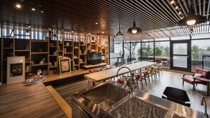 A modern kitchen with a large stainless steel sink, wooden shelves with books, and a dining area with a long table and chairs. - 3 Door Hotel (Tainan)