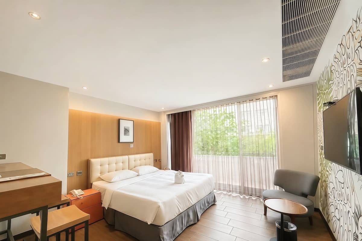 A hotel room with a bed, a desk, a chair, a TV, and a window with curtains.