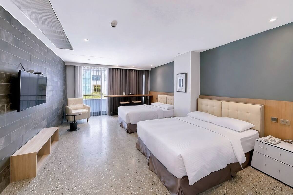 A modern hotel room with a large bed, a smaller bed, a sofa, a TV, a desk, and a window with curtains.