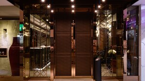 A modern interior with a central elevator, glass partitions, and a reception area with a counter and chairs. - 3 Door Hotel (Tainan)