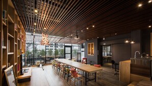 A modern interior with a long wooden table, multiple chairs, and a kitchen area. - 3 Door Hotel (Tainan)