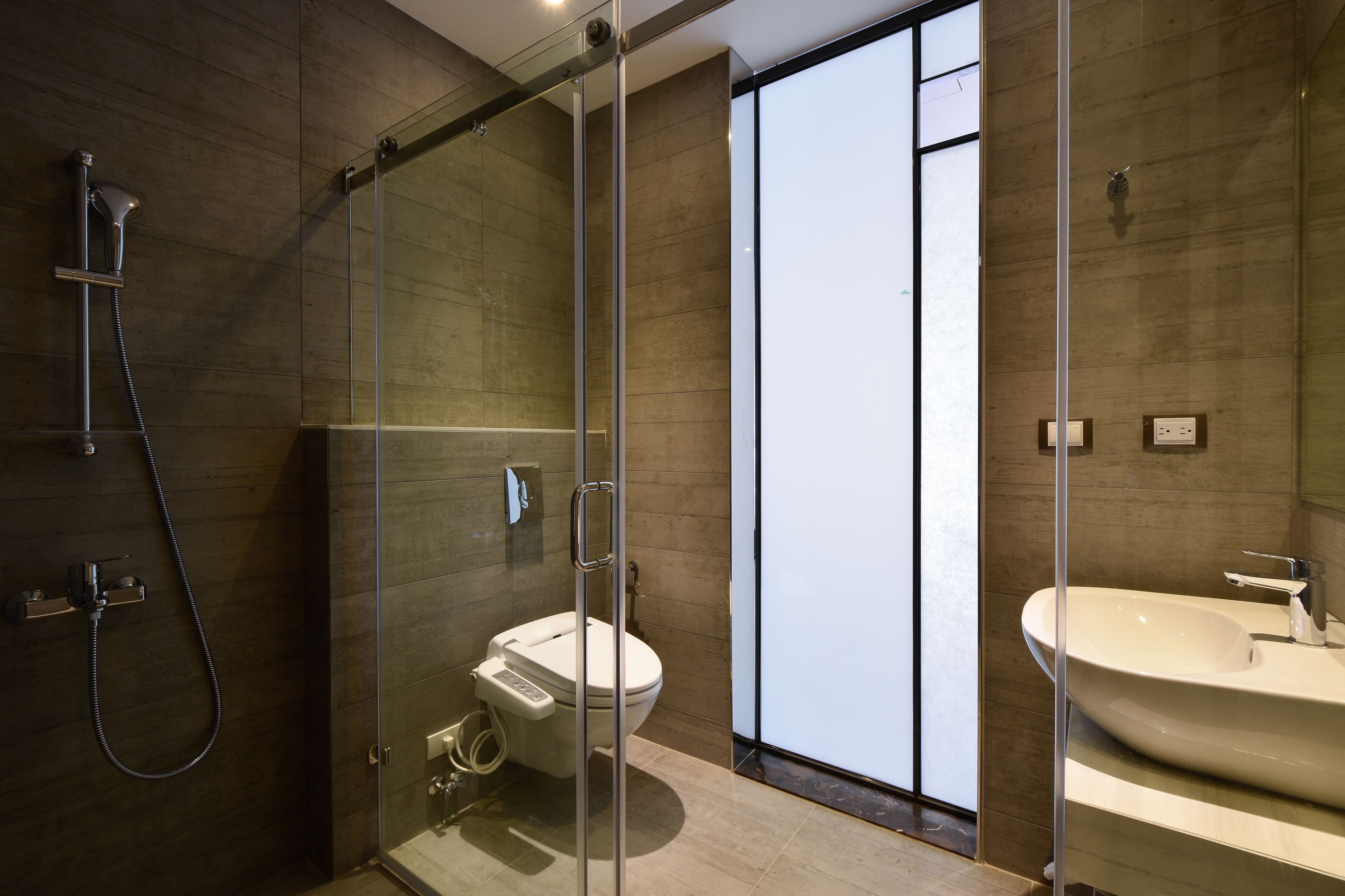 A modern bathroom with a glass-enclosed shower, a toilet, and a sink.