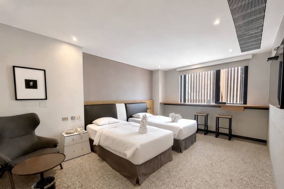A hotel room with two beds, a sofa, a small table, a nightstand, and a window with blinds.