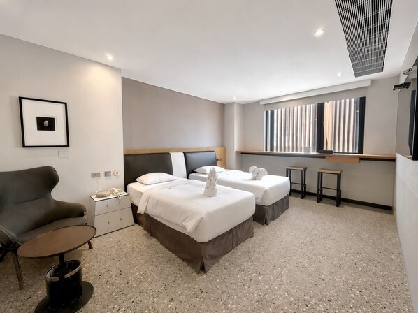 A hotel room with two beds, a sofa, a small table, a nightstand, and a window with blinds. - 3 Door Hotel (Tainan)