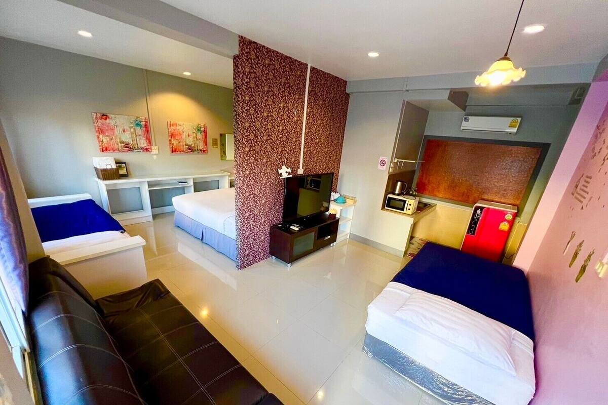 A modern hotel room with two beds, a sofa, a TV, a microwave, and a kitchenette.