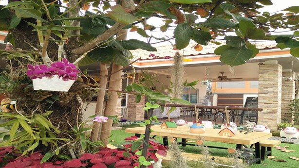 A garden with a wooden table, hanging plants, and a house-shaped decoration. - Winhouse Hotel (Nan)