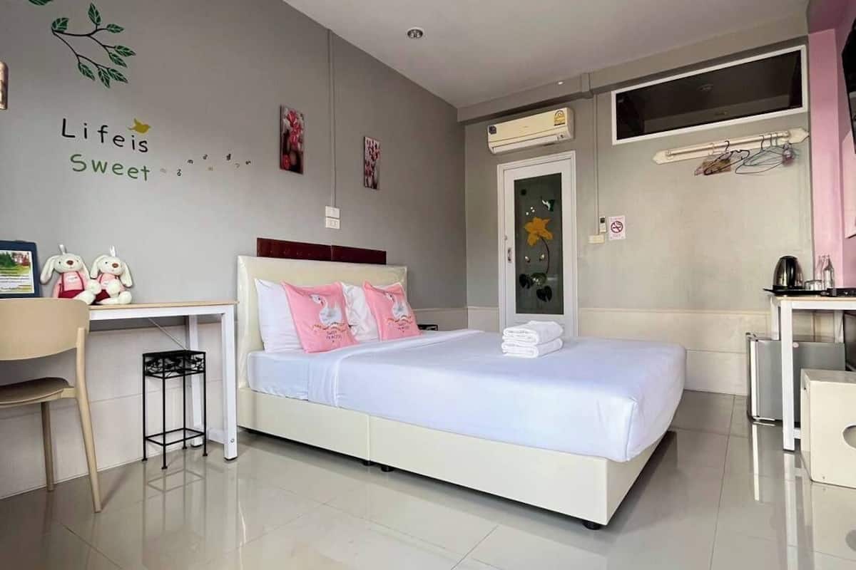 A modern bedroom with a bed, a desk, and a chair. There is a wall decoration with the text "Life is Sweet" and a small window above the bed.