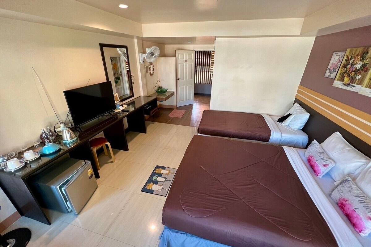 A hotel room with two beds, a desk with a computer, a TV, and a small kitchenette.