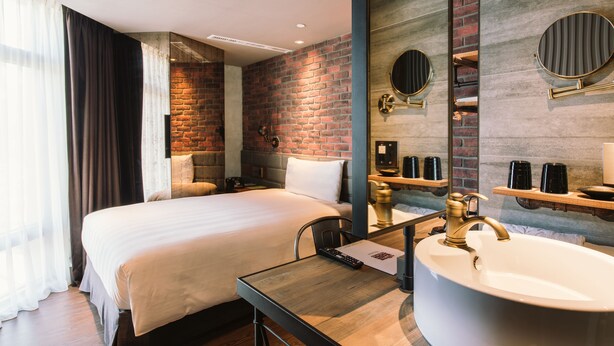 A modern hotel room with a large bed, a wooden desk, a round mirror, and a large bathtub.
