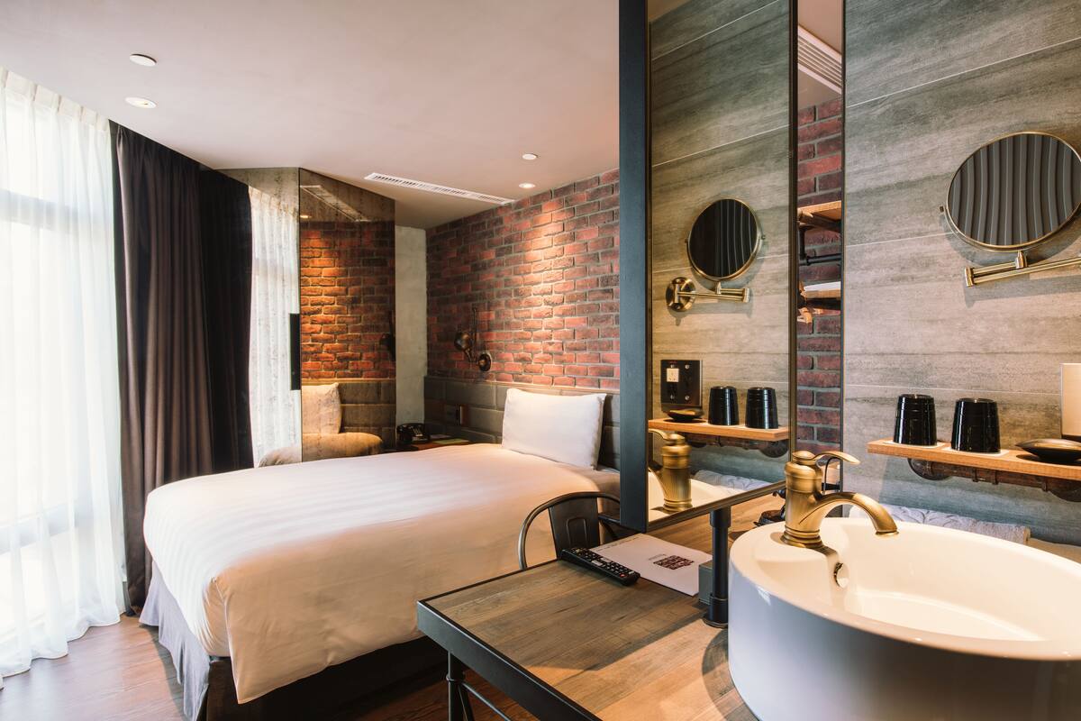 Ein modernes Hotelzimmer mit einem großen Bett, einem Holztisch, einem runden Spiegel und einer großen Badewanne.