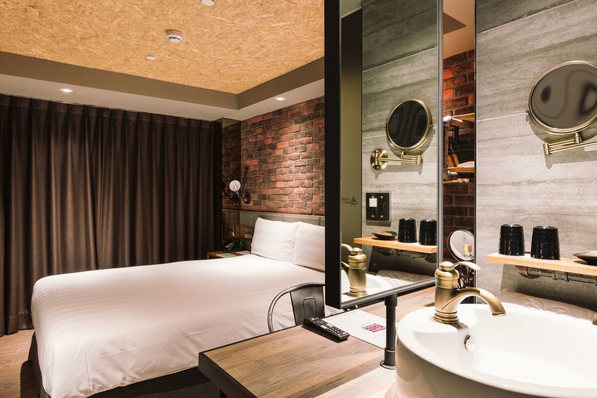 Ein Hotelzimmer mit Bett, Schreibtisch, Spiegel und einem Badezimmer mit Waschbecken und Spiegel.