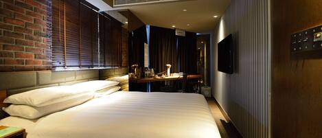 Habitación de hotel con una cama grande, un escritorio con una silla, un televisor montado en la pared y una pared de ladrillo.