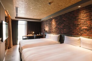 Una camera d'albergo con due letti, un muro in mattoni, una scrivania in legno e un televisore.