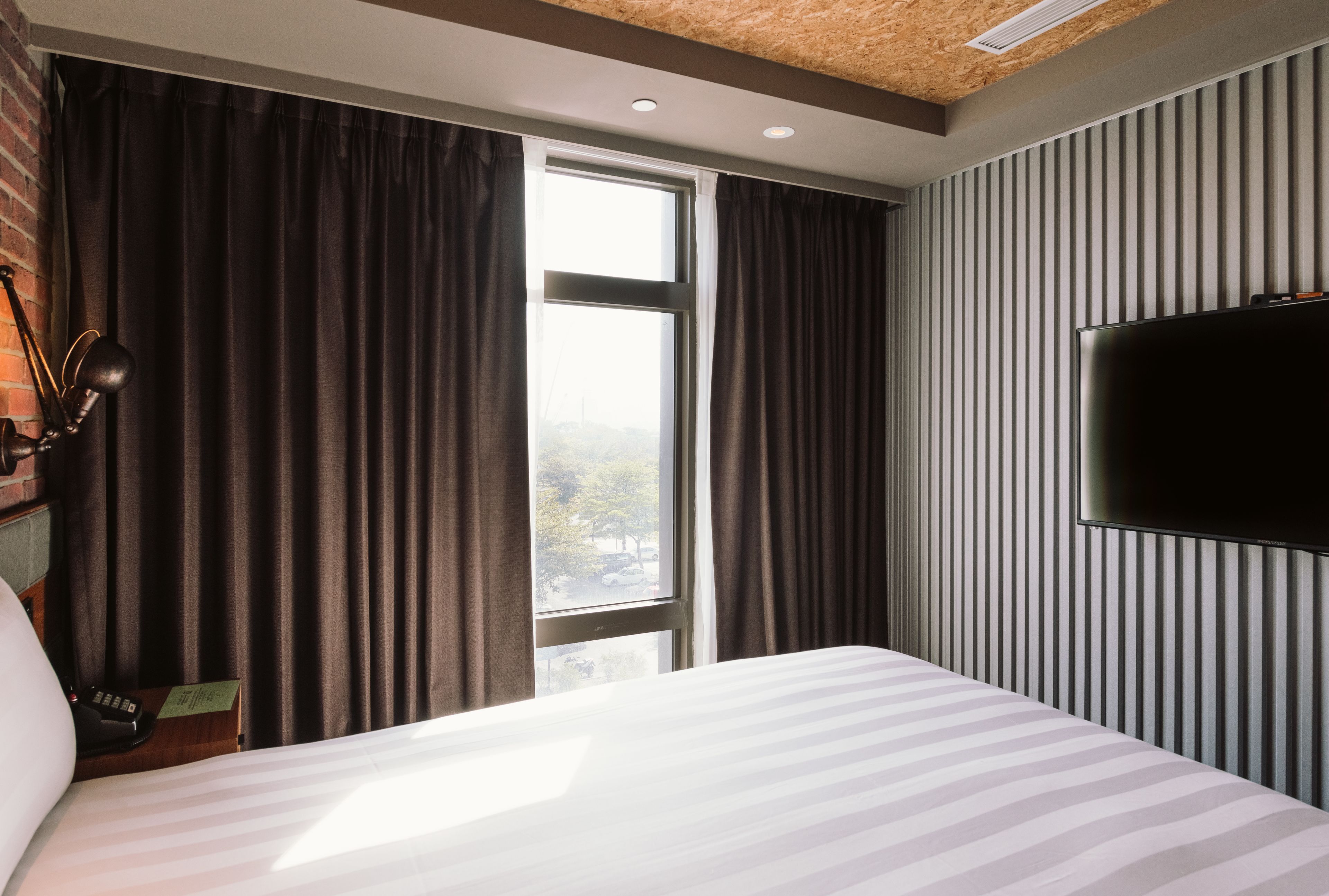 A hotel room with a large bed, a flat-screen TV mounted on the wall, and a window with curtains.