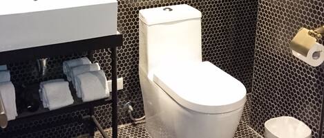 Baño con pared de patrón hexagonal blanco y negro, un lavamanos con artículos de aseo, un inodoro y un cubo de basura pequeño.