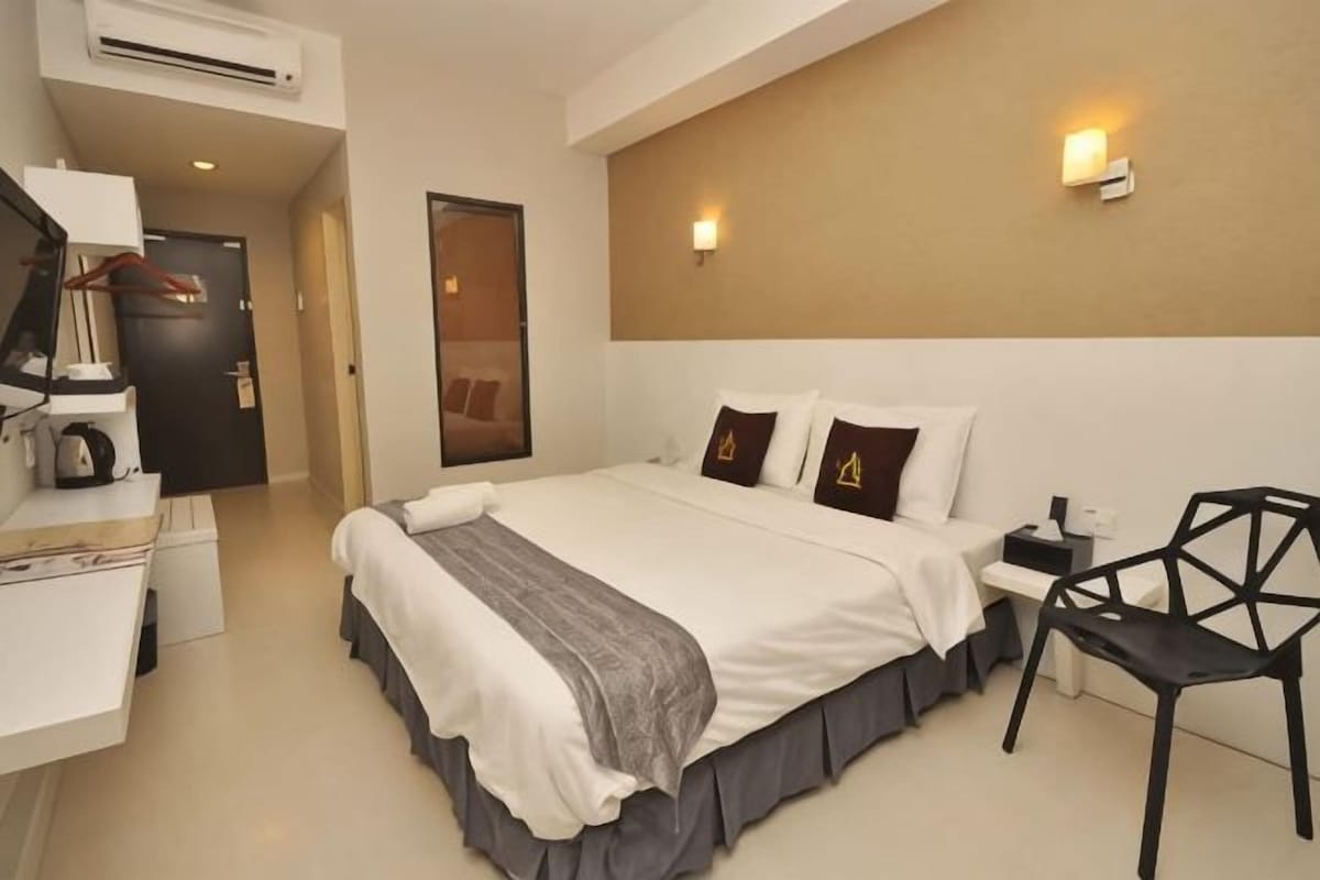 Quarto de hotel com cama, mesa de cabeceira, cadeira, escrivaninha e espelho.