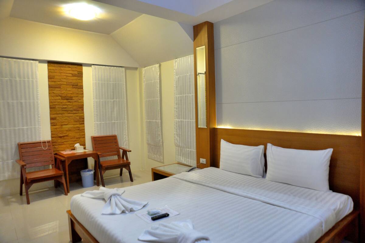 Habitación de hotel con una cama grande, dos sillas de madera, una mesita pequeña y un muro decorativo de piedra.
