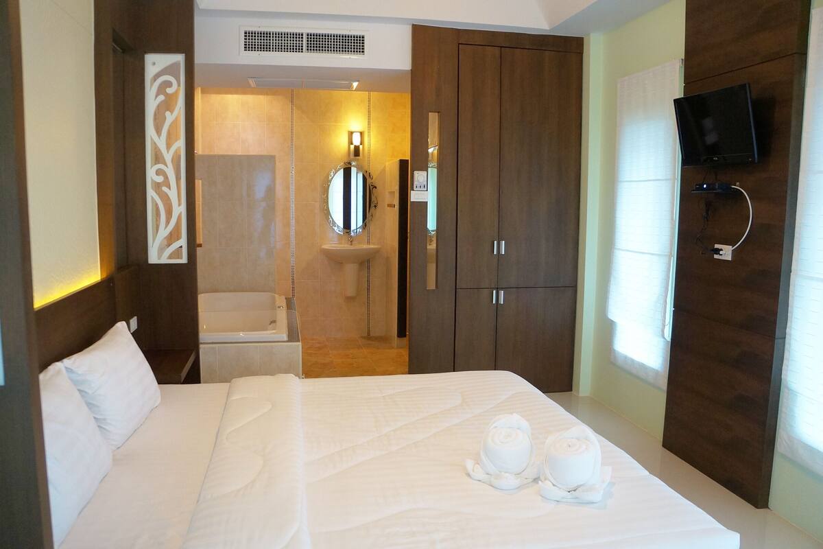 Habitación de hotel con cama, baño con lavamanos, espejo y televisor montado en la pared.