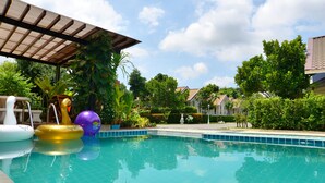 A clear swimming pool with inflatable toys, surrounded by lush greenery and residential buildings. - Chanpraya Resort (Chanthaburi)