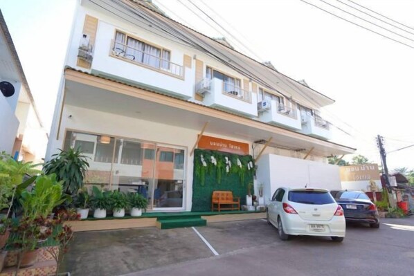 Un edificio de dos pisos con un toldo verde y un letrero que dice 'Kahluah House'. Hay plantas en macetas al frente y un coche blanco estacionado en la entrada.