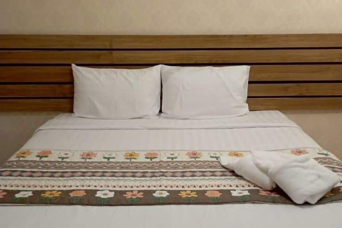 A bed with a wooden headboard, two white pillows, and a floral-patterned bedspread.