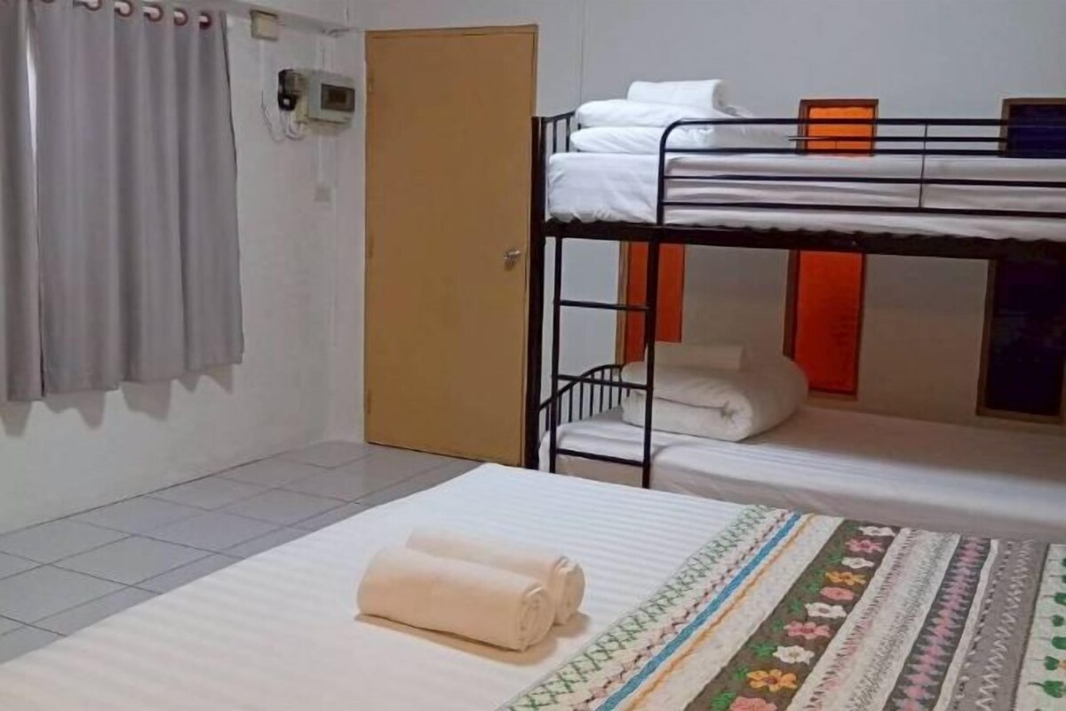 A bunk bed room with a door, a window with curtains, and a bed with a patterned blanket.
