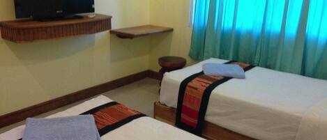 A hotel room with two beds, a TV on a shelf, a small table, and a window with curtains.
