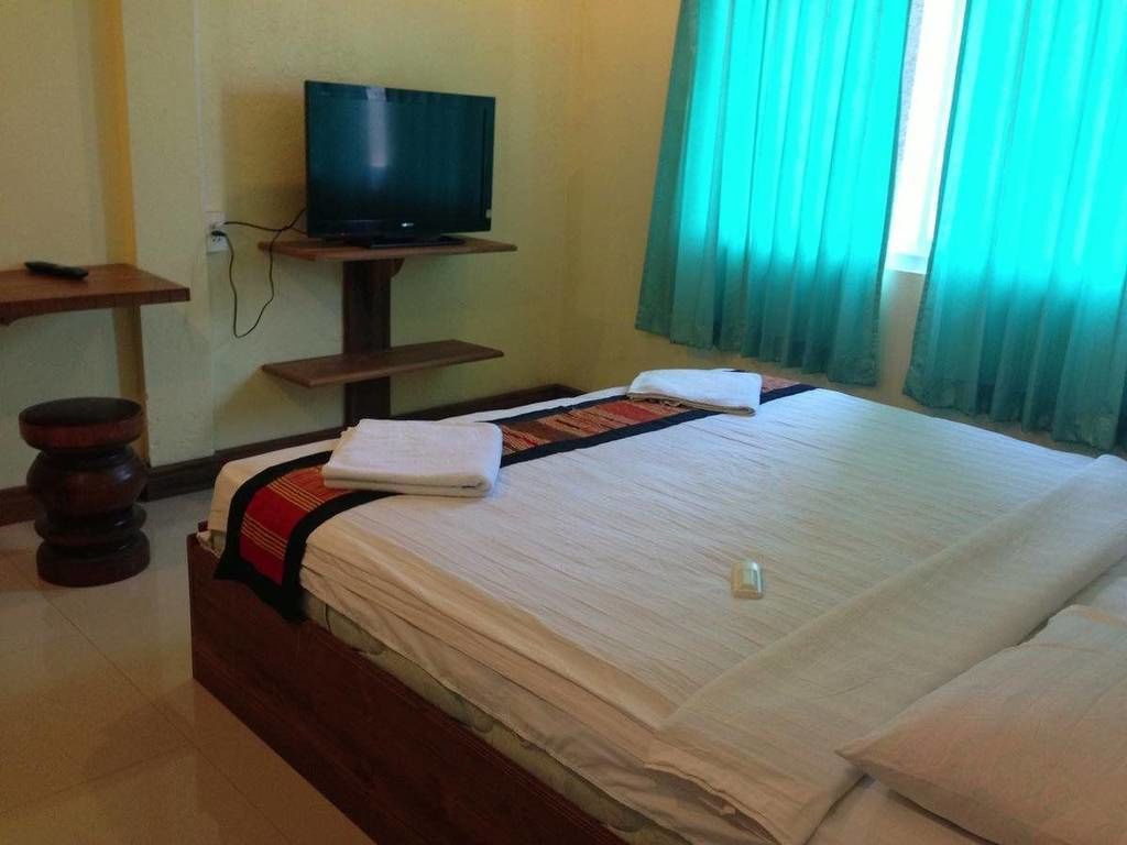 A hotel room with a bed, a television on a stand, a bedside table, and a window with curtains.