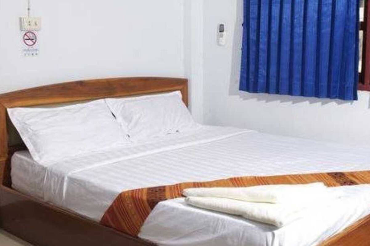 Uma cama de solteiro com estrutura de madeira, roupa de cama branca e um cobertor listrado.