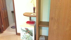 A wooden cabinet with a shelf containing a vase, a red tray, and a pair of slippers. - Lankham Hotel (Pakse)