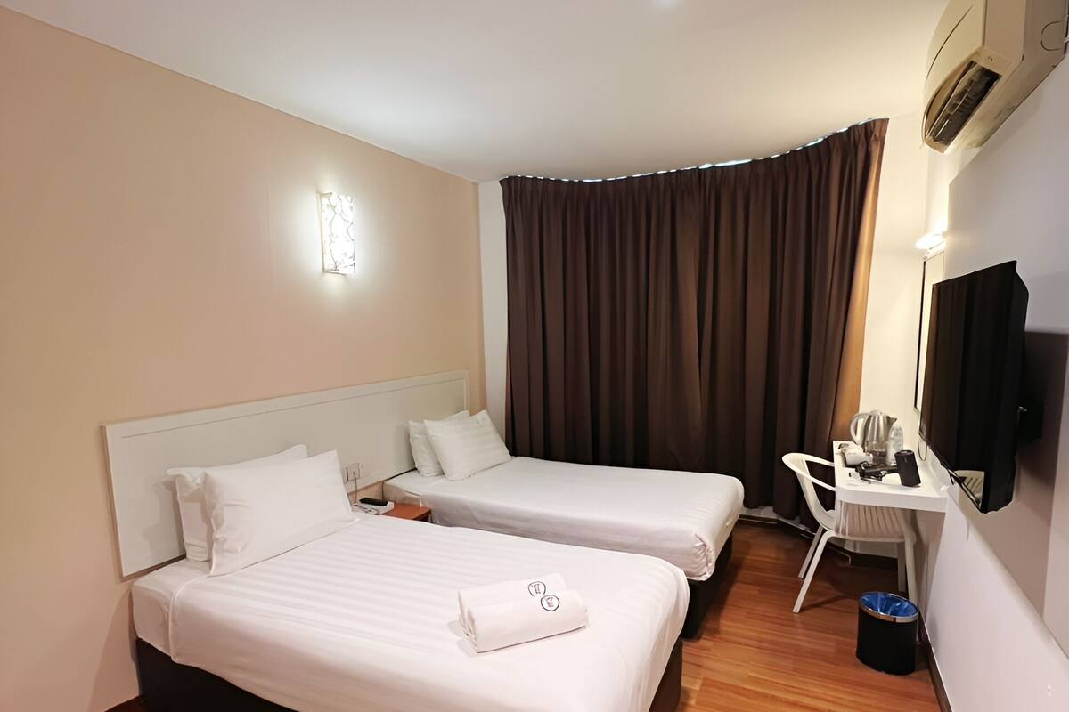 A hotel room with two beds, a desk, a chair, a TV, and a ceiling-mounted air conditioner.