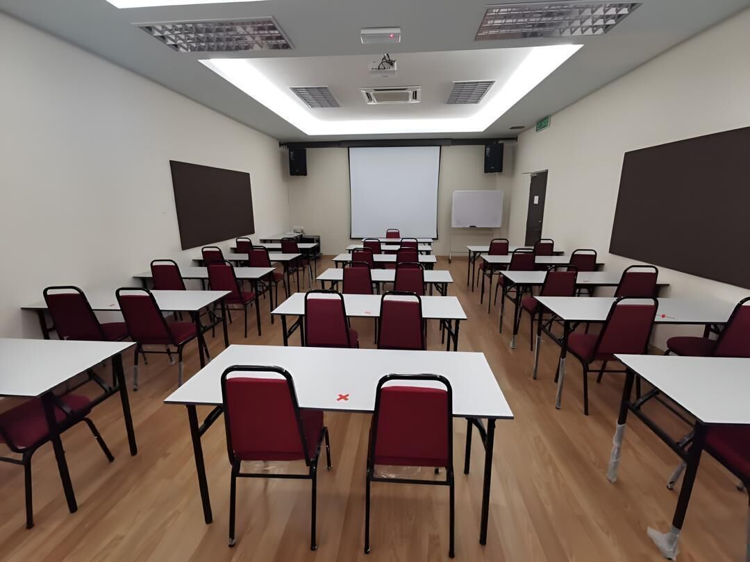 Un aula con filas de escritorios y sillas, una pantalla de proyector y una pizarra.