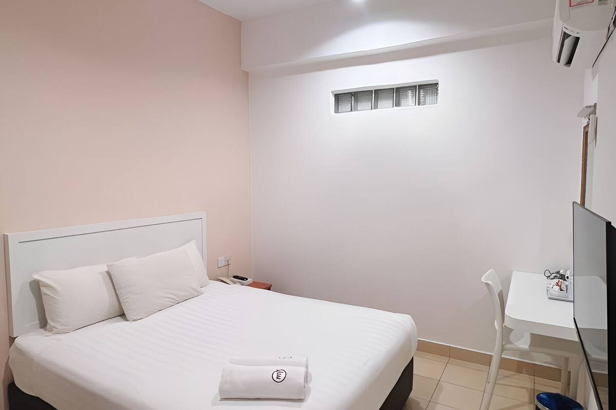 A hotel room with a large bed, a small desk, a television, and a window with blinds.