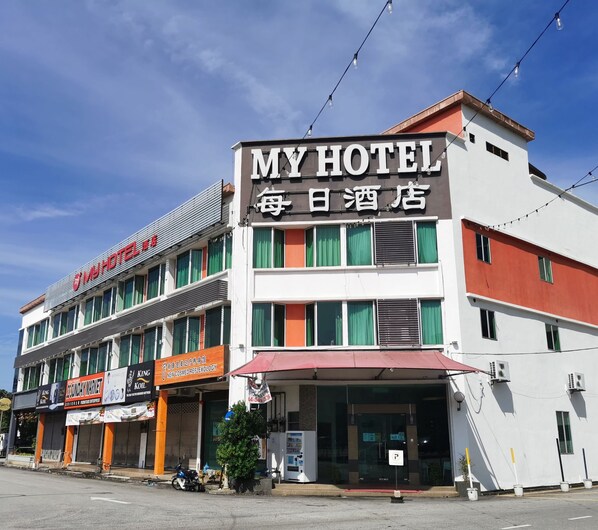 Un hôtel avec une enseigne indiquant « MON HÔTEL » et « HÔTEL OUVERT TOUS LES JOURS ».