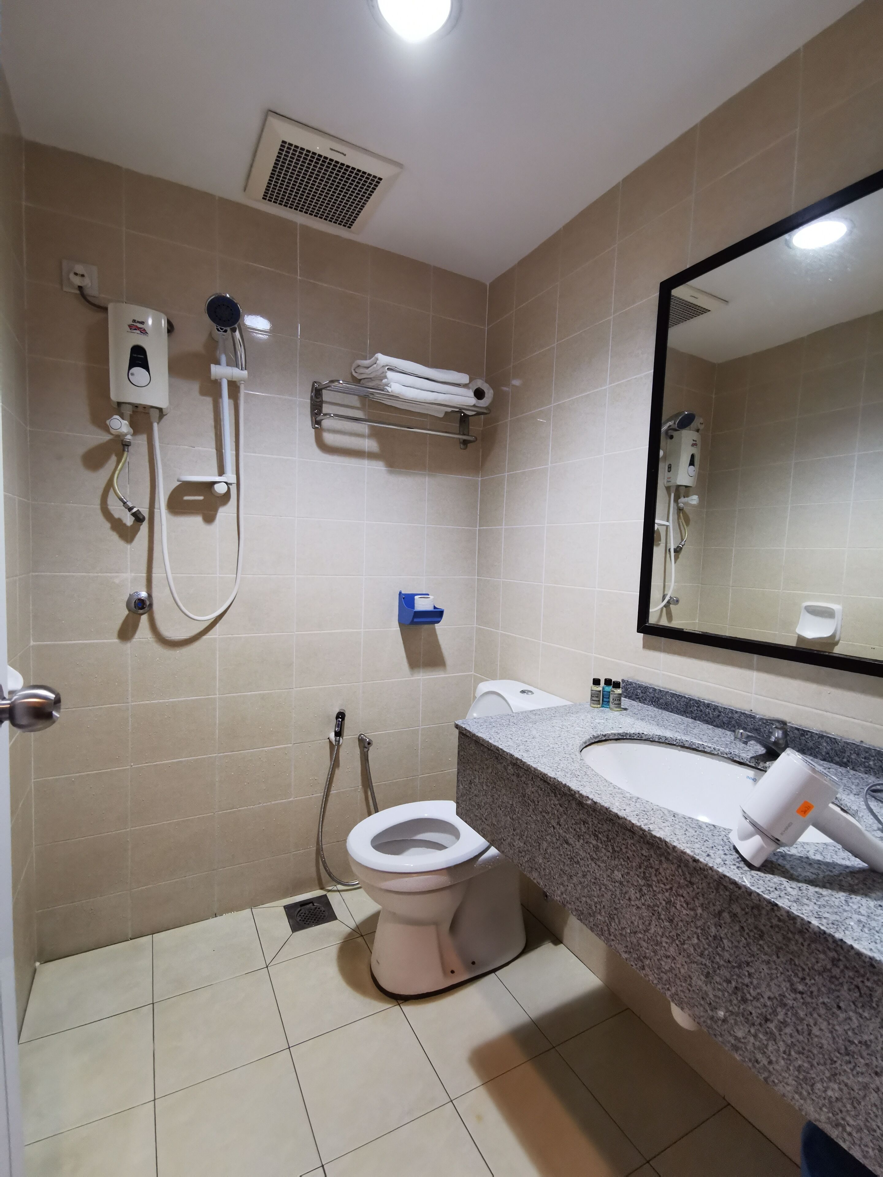 A bathroom with a toilet, sink, mirror, towel rack, and shower unit.