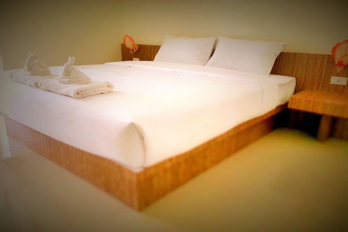 Ein ordentlich bezogenes Bett mit weißen Bettwäsche und Handtüchern, ein Holz-Kopfbrett und ein Nachttisch mit Lampe.