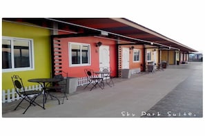 Una hilera de edificios coloridos con espacios al aire libre, cada uno con un cercado de piquetes blancos y un conjunto de mesa y sillas.