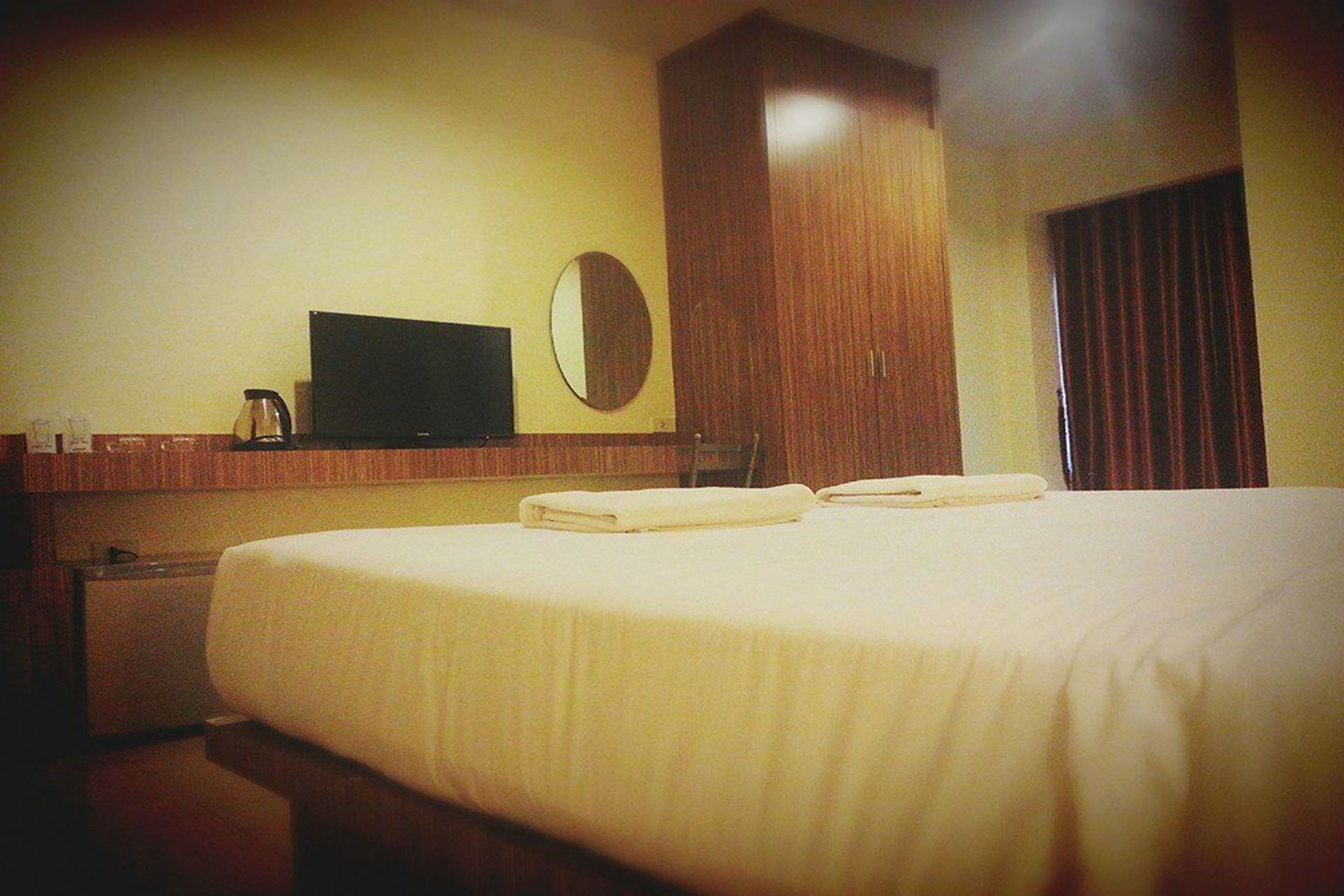 Una habitación de hotel con cama, televisor, espejo y armario.