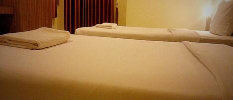 Two single beds with white linens and a wooden wardrobe in the background.