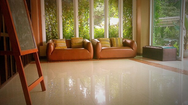 A spacious room with a large window, a brown sofa set, and a wooden easel. - Le Luxe Residence (Udon Thani)