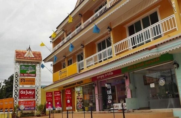 A multi-story building with balconies, storefronts, and a signboard with business names and contact information. - Chinatip Yusabuy (Nan)