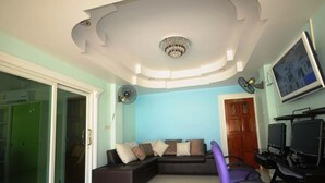Una sala de estar con un sofá modular, un sillón morado, un televisor y un ventilador de techo.