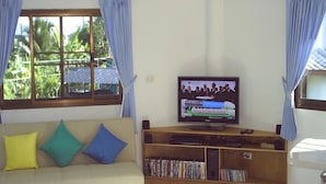 A living room with a sofa, TV, and a wooden entertainment unit with DVDs. - Ban Rim Nam Riverside Resort (Nan)