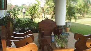 A wooden outdoor seating area with a table and chairs, surrounded by potted plants and a view of a garden.