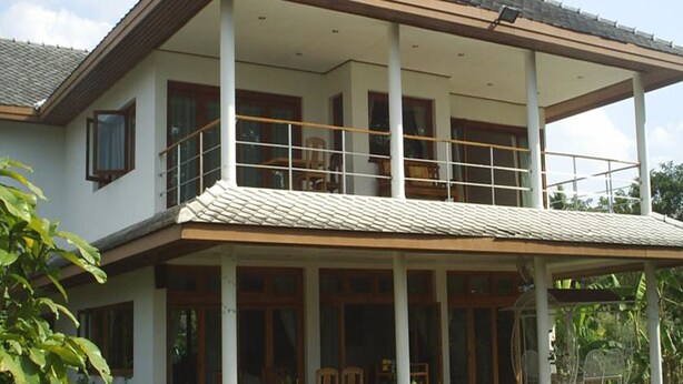 A two-story house with a balcony, large windows, and a tiled roof.
