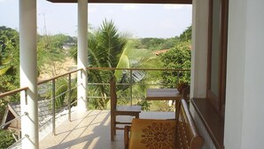 A balcony with a wooden table and chairs, a view of a river and greenery, and a tiled floor.