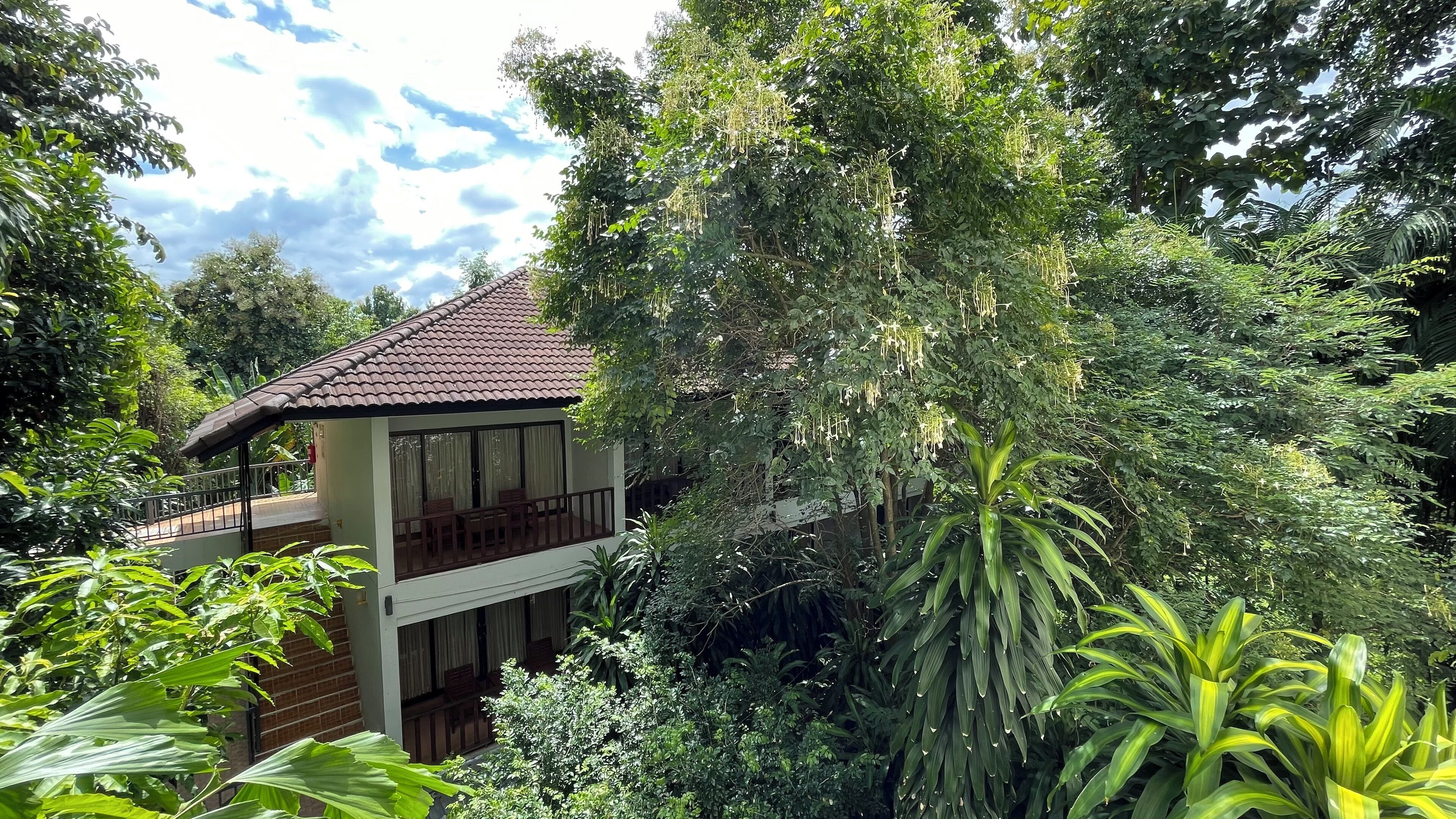 A two-story house with a tiled roof, surrounded by dense greenery and trees.